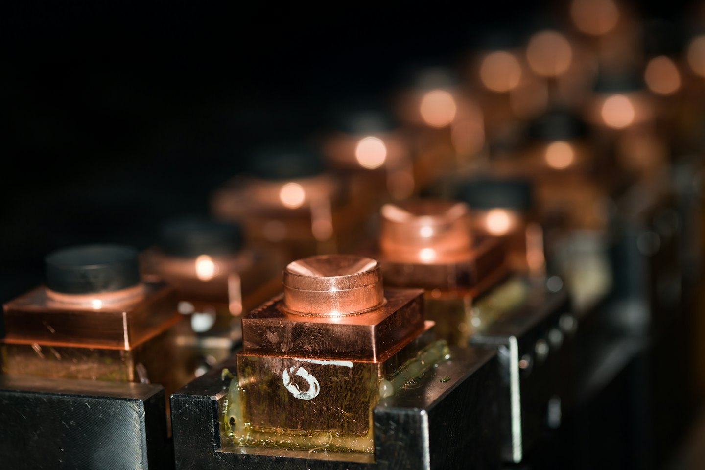 Precision machined copper components secured in a metal workbench fixture.