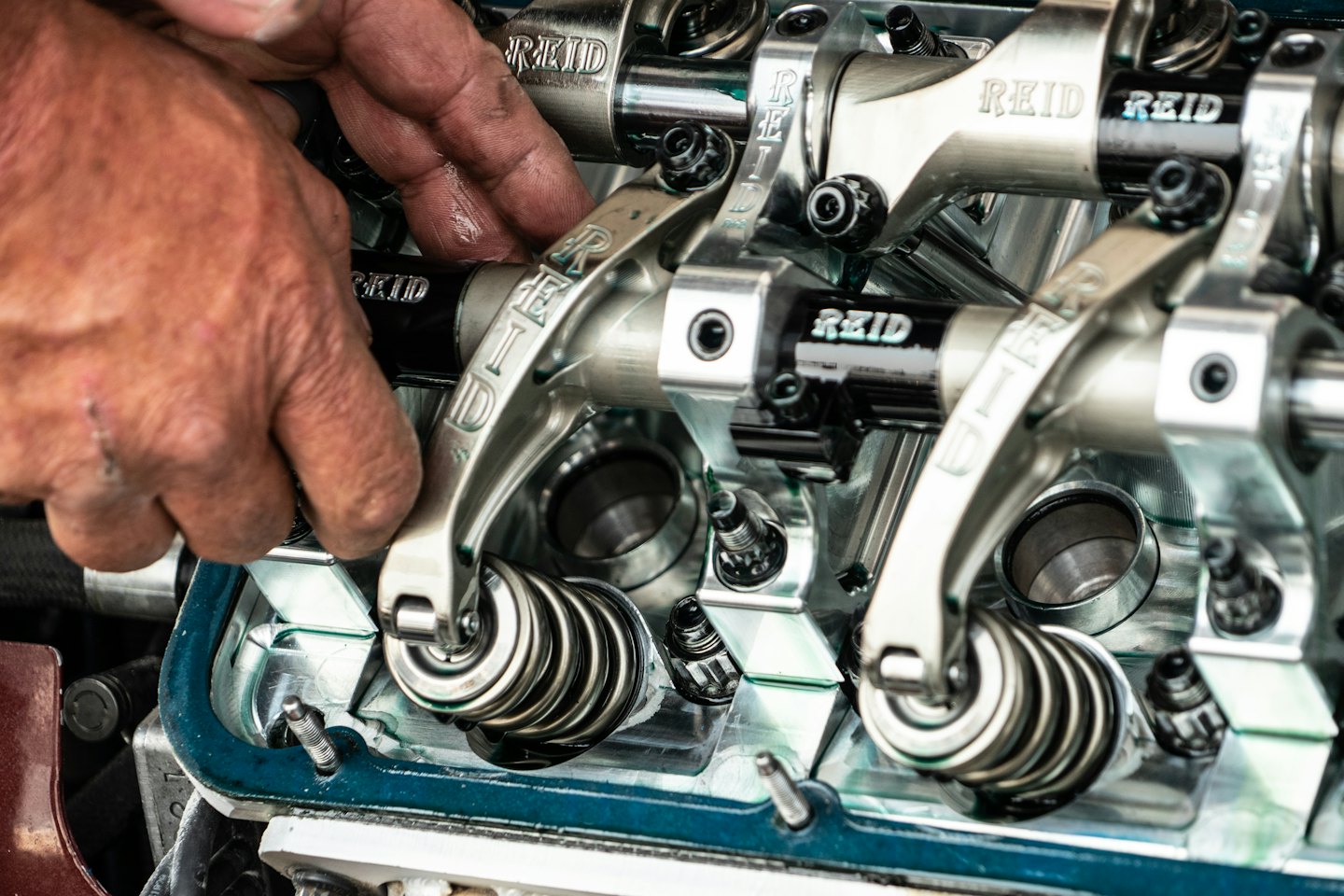 Hand assembling intricate engine components with rocker arms and valve springs.